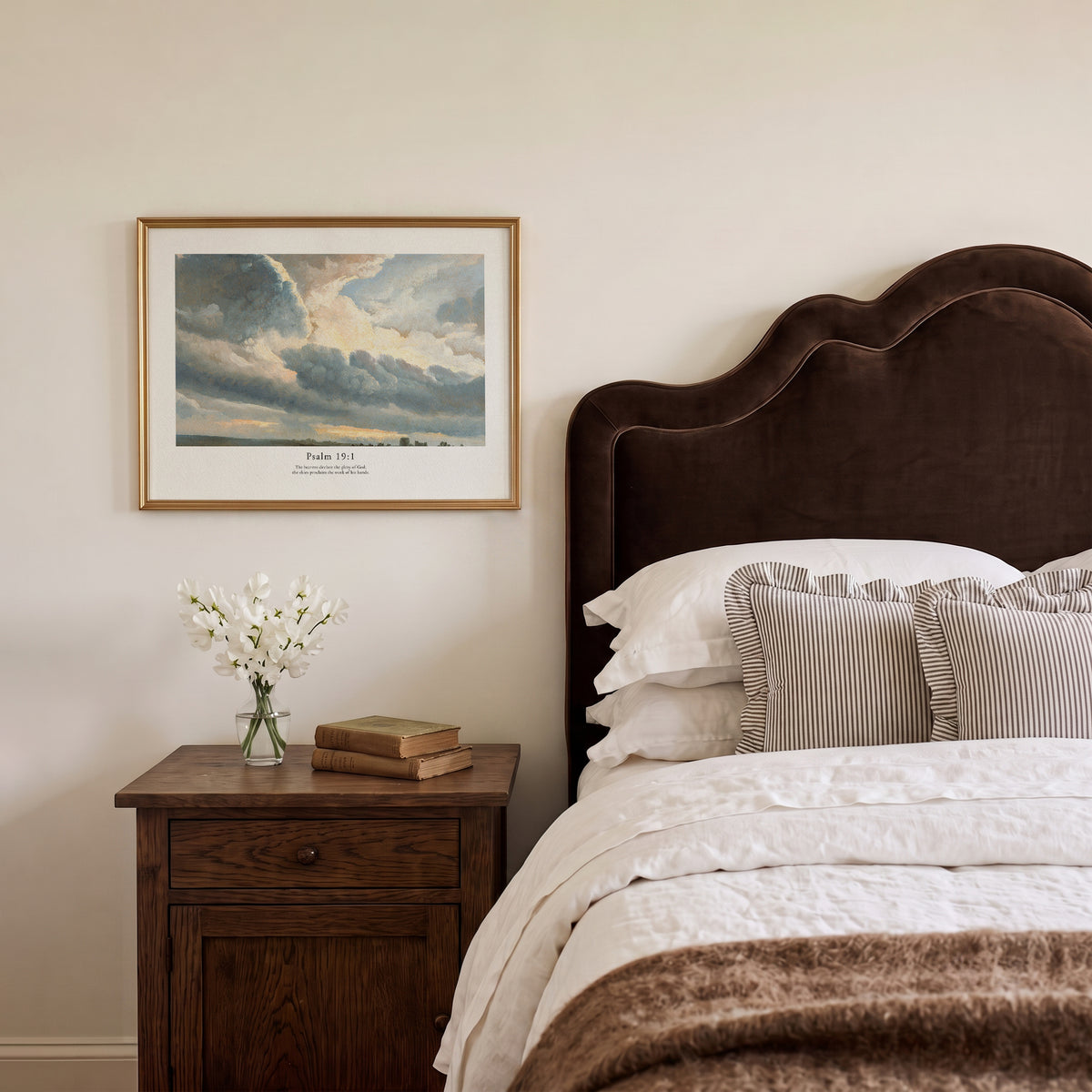 Christian wall art featuring Psalm 19:1 and a dramatic sky painting, styled above a wooden bedside table.