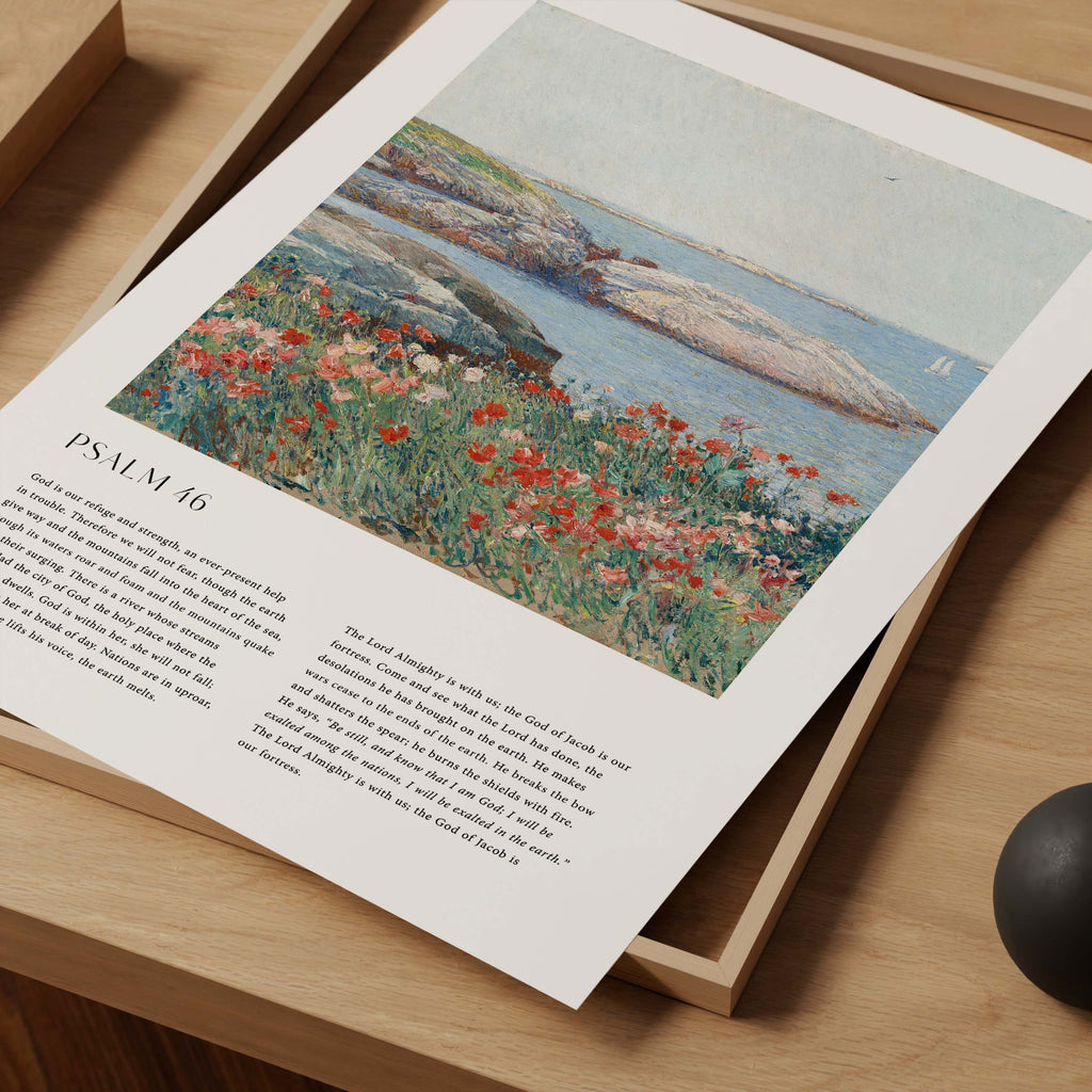 A printed art print featuring a coastal landscape painting with red and white flowers in the foreground, resting on a light wood tray over a wooden surface.