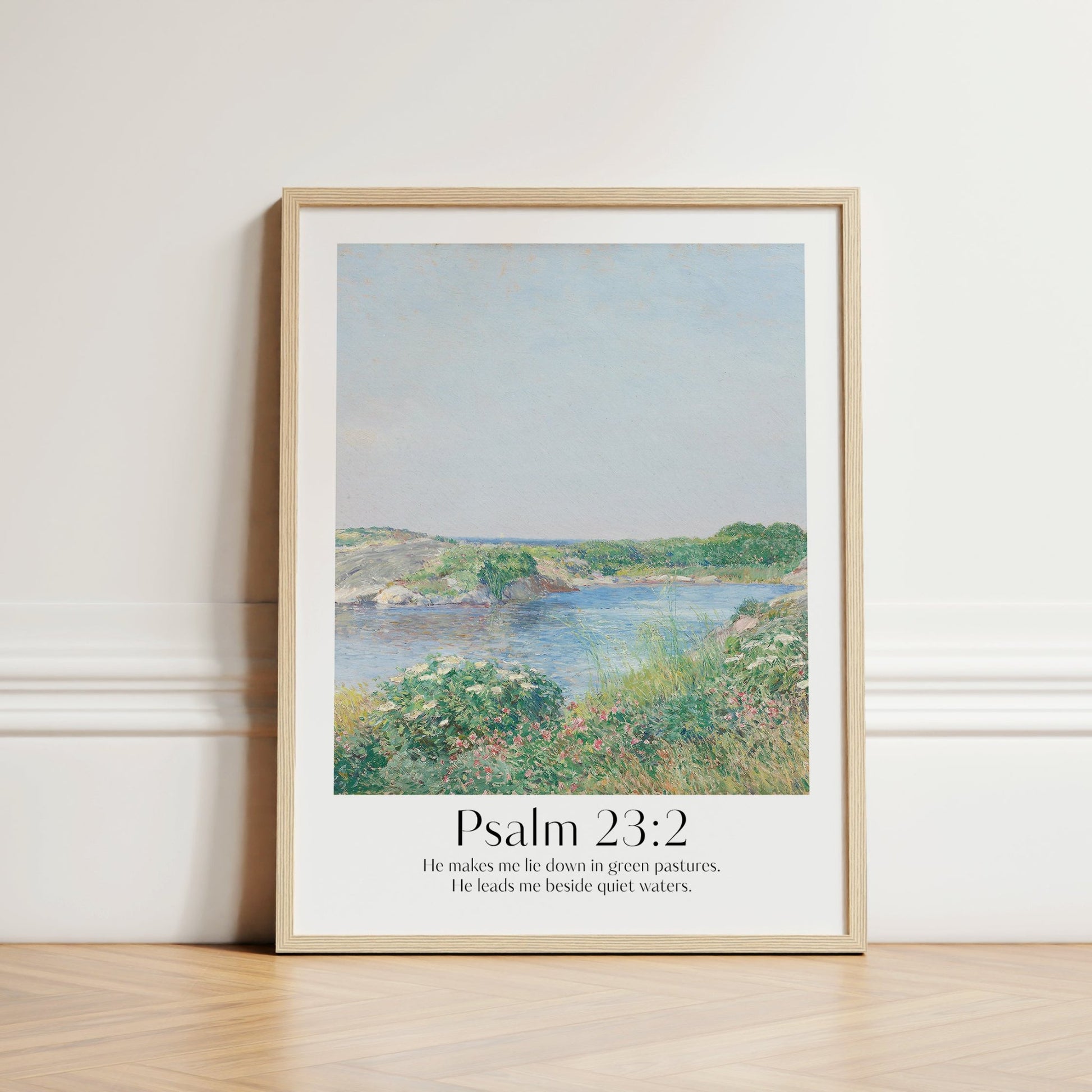 Framed Christian wall art print inspired by Childe Hassam, featuring a serene landscape with natural light and shadows. Displays the Bible verse Psalm 23:2: "He makes me lie down in green pastures. He leads me beside quiet waters." This artwork combines a peaceful, impressionist-style landscape with comforting scripture, making it a tranquil addition to any Christian home. Elegantly framed in light wood, perfect for enhancing living room or bedroom decor.