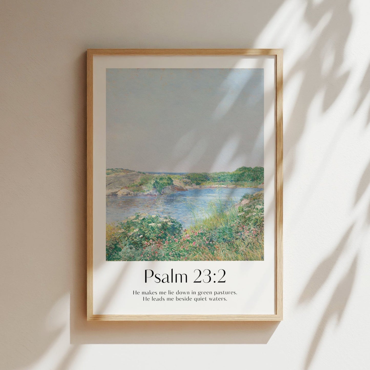 Framed Christian wall art print featuring a serene landscape inspired by Childe Hassam. Displays the Bible verse Psalm 23:2: "He makes me lie down in green pastures. He leads me beside quiet waters." This artwork combines a peaceful, impressionist-style landscape with comforting scripture, making it a tranquil addition to any Christian home. Elegantly framed in light wood, ideal for enhancing living room or bedroom decor.