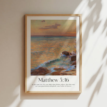 Framed Christian wall art print featuring a stunning coastal sunset scene inspired by Menci Clement. The artwork displays a serene ocean view at dusk, with gentle waves lapping against the rocks, paired with the Bible verse Matthew 5:16: "In the same way, let your light shine before others, that they may see your good deeds and glorify your Father in heaven." This piece combines beautiful scenery with a message of spiritual encouragement, making it a thoughtful addition to any home or prayer space.